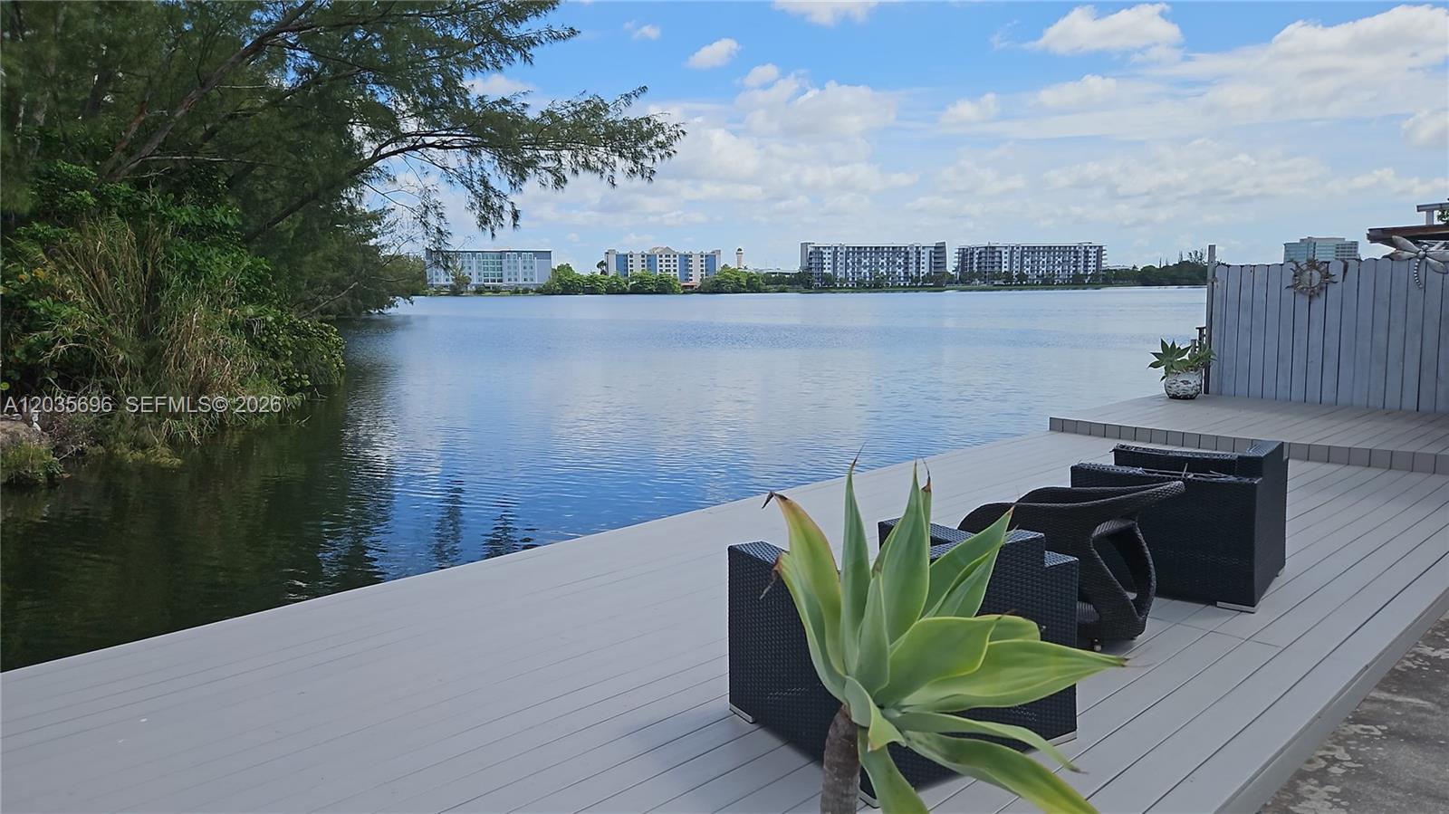 A wooden deck with outdoor furniture overlooks a lake with distant apartment buildings — 6895 Tamiami Canal Rd, Miami FL 33126, MIAMI, FL