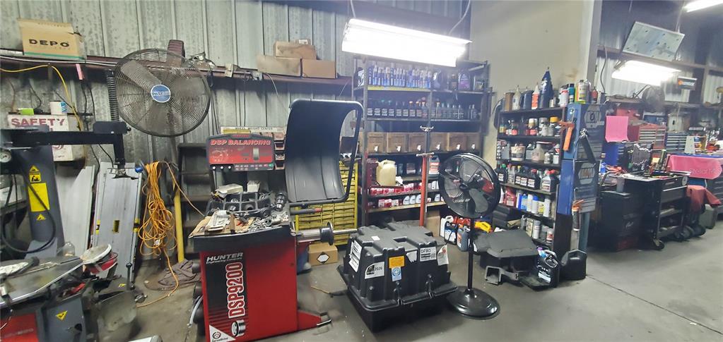A cluttered automotive repair shop features a Hunter wheel balancer, shelving units, and industrial fans — 2714 ORLANDO, SANFORD, FL