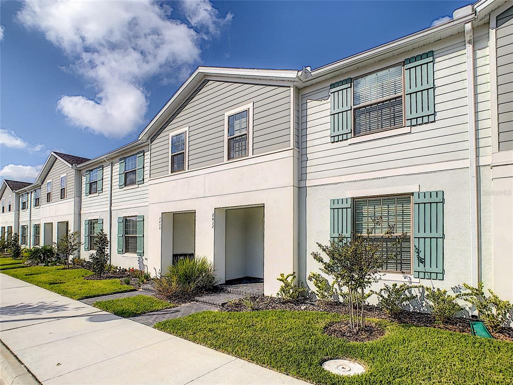 A row of two-story townhomes with light-colored siding, stucco walls, and green window shutters — 2430 TANGIER DRIVE, KISSIMMEE, FL