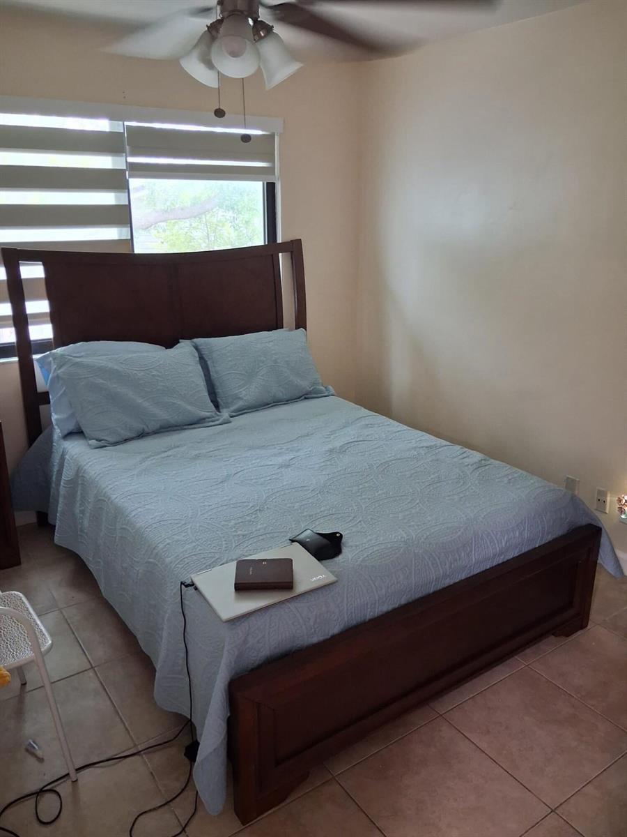 A bedroom features a wooden bed frame with a light blue quilt and a ceiling fan — 9752 NW 37th Street # 7g, Sunrise FL 33351, SUNRISE, FL