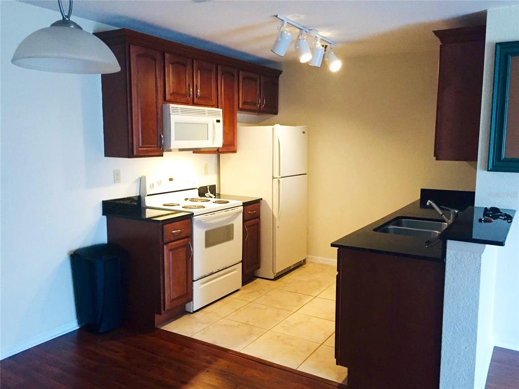 A kitchen with dark wood cabinets, white appliances, black countertops, and light tile flooring — 10263 GANDY BOULEVARD N UNIT 513, ST PETERSBURG, FL