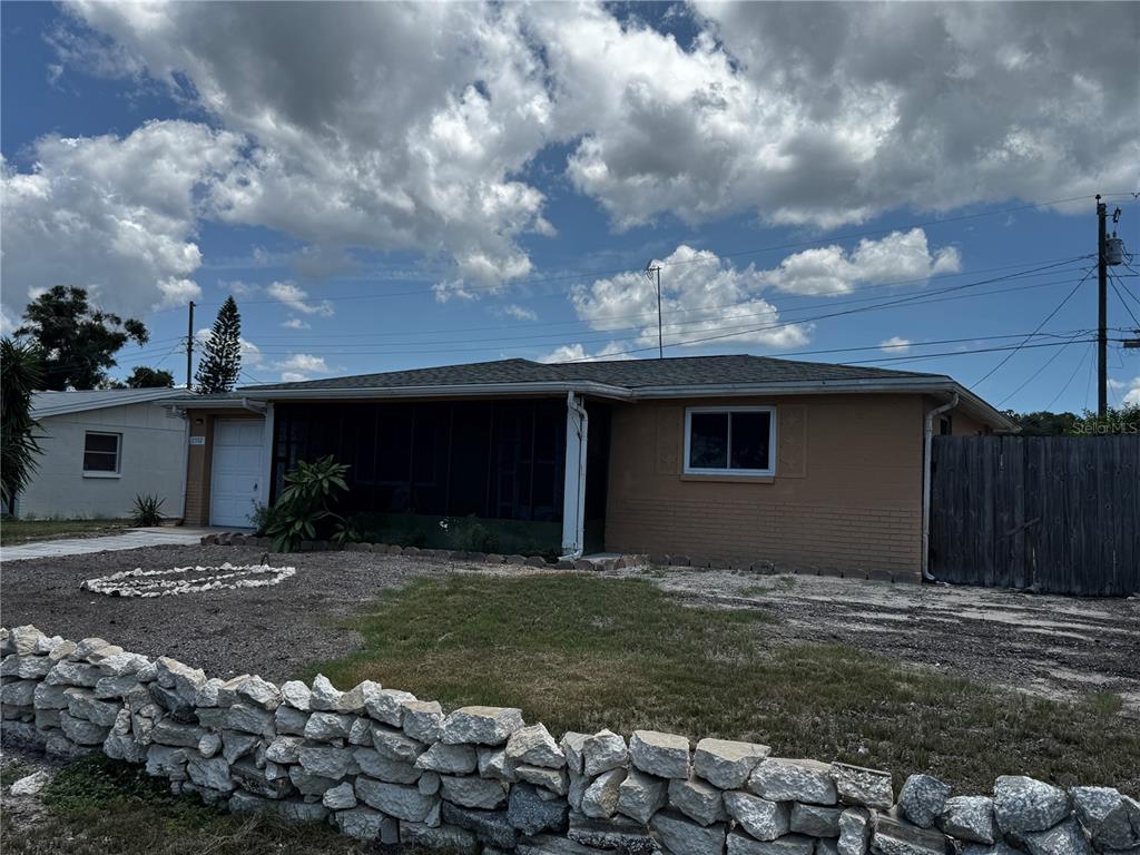 A single-story house with a tan brick exterior, a screened porch, and a stone wall — 2552 LIMEWOOD DRIVE, HOLIDAY, FL