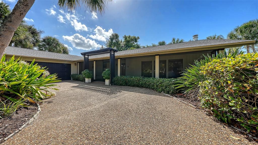 A single-story house with a gravel driveway, a dark garage door, and a wooden pergola — 5345 SIESTA COURT, SARASOTA, FL