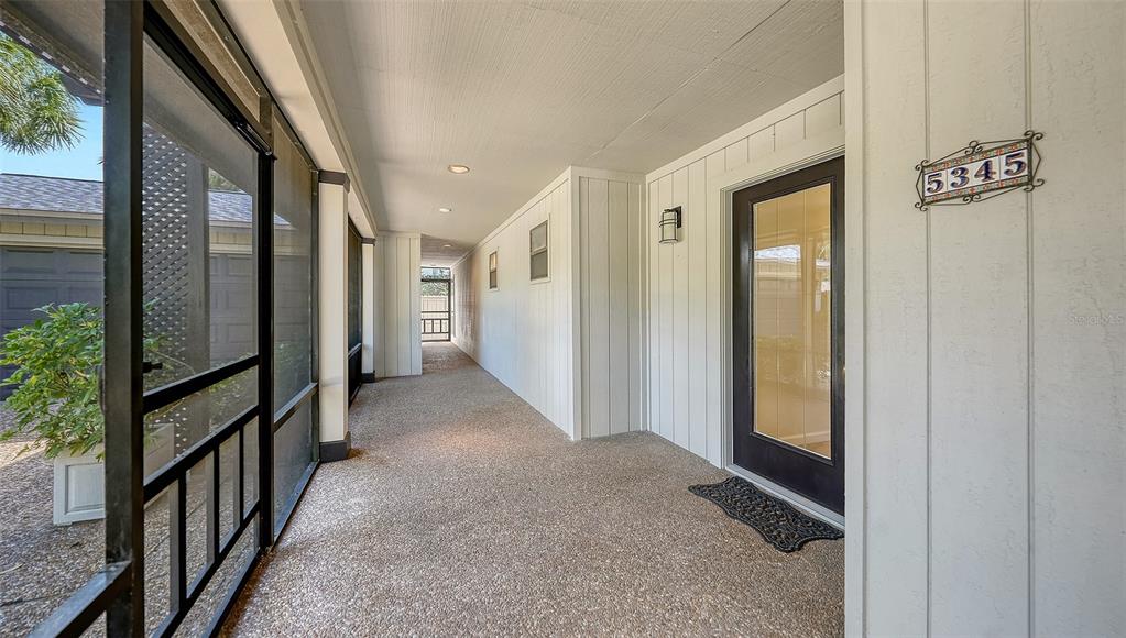 A covered, screened-in porch features a concrete floor and a dark-framed glass front door — 5345 SIESTA COURT, SARASOTA, FL