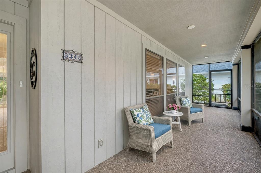 A screened-in porch features light-colored vertical siding, two wicker chairs, and a small side table — 5345 SIESTA COURT, SARASOTA, FL