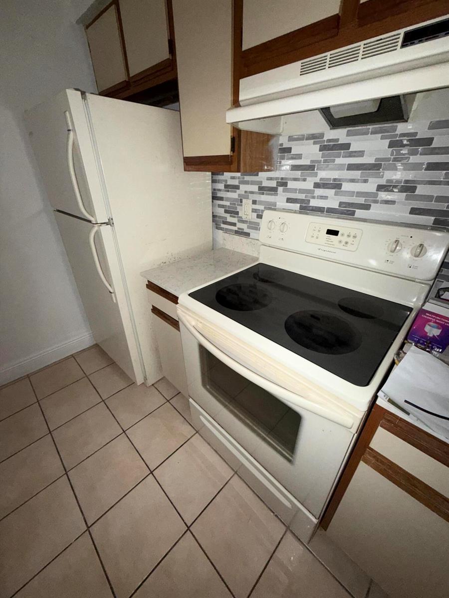 A kitchen features a white refrigerator, electric stove, and a gray and white tiled backsplash — 1285 SW 46th Avenue # 2709, Pompano Beach FL 33069, POMPANO BEACH, FL