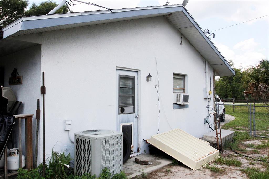 The exterior of a white stucco house features an air conditioning unit and a door — 7615 N LAZY TRAIL, CRYSTAL RIVER, FL