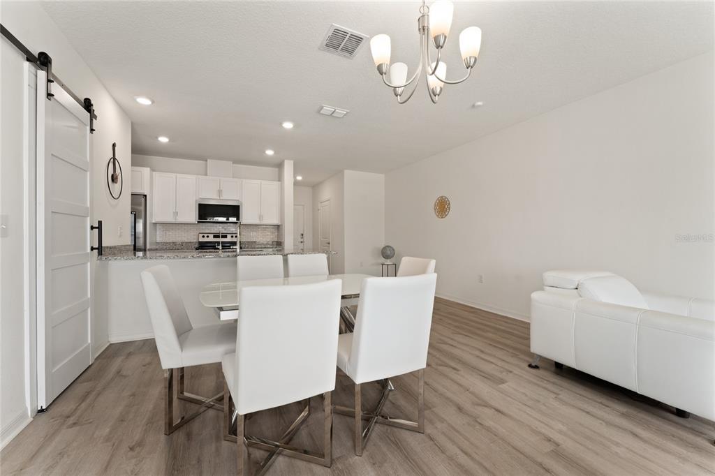 A dining area with white chairs and a chandelier sits adjacent to a modern kitchen — 697 STONEY POINT CIRCLE, DAVENPORT, FL