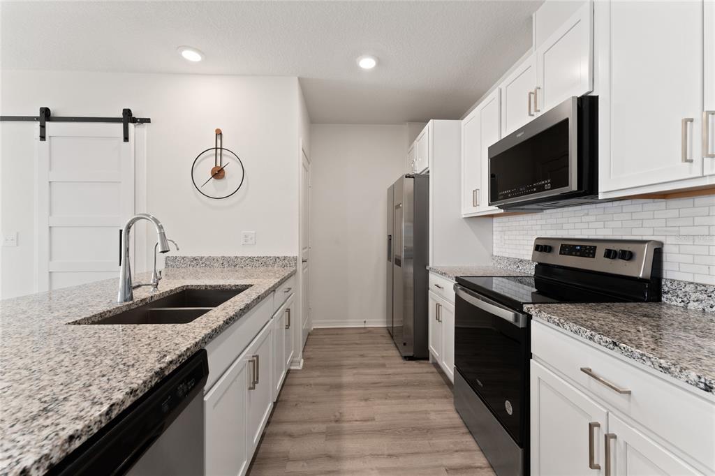A kitchen features white cabinets, granite countertops, stainless steel appliances, and wood-look flooring — 697 STONEY POINT CIRCLE, DAVENPORT, FL