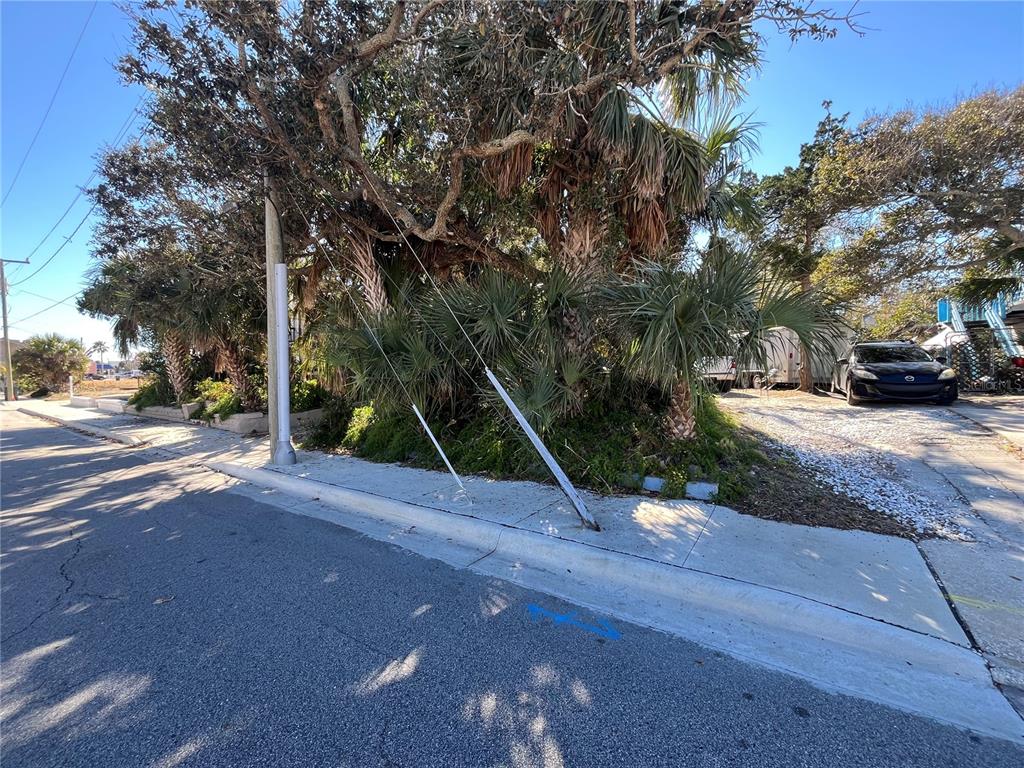 A utility pole with support wires stands on a sidewalk next to a gravel driveway — N HOLLYWOOD AVENUE, DAYTONA BEACH, FL