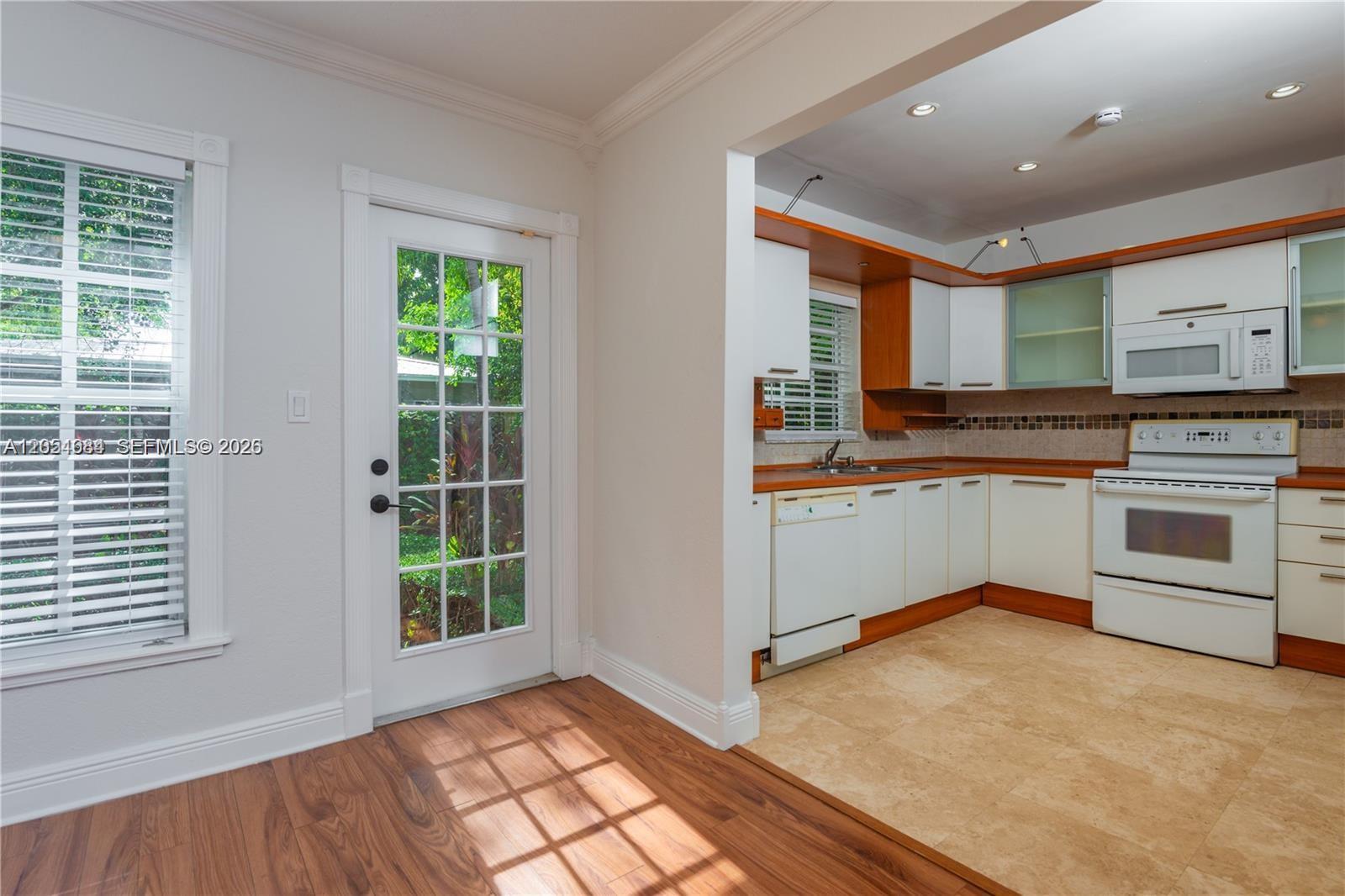A kitchen with white cabinets, wood trim, and tile flooring connects to a wood-floored room — 5490 SW 57 Ave # 0, Miami FL 33155, MIAMI, FL