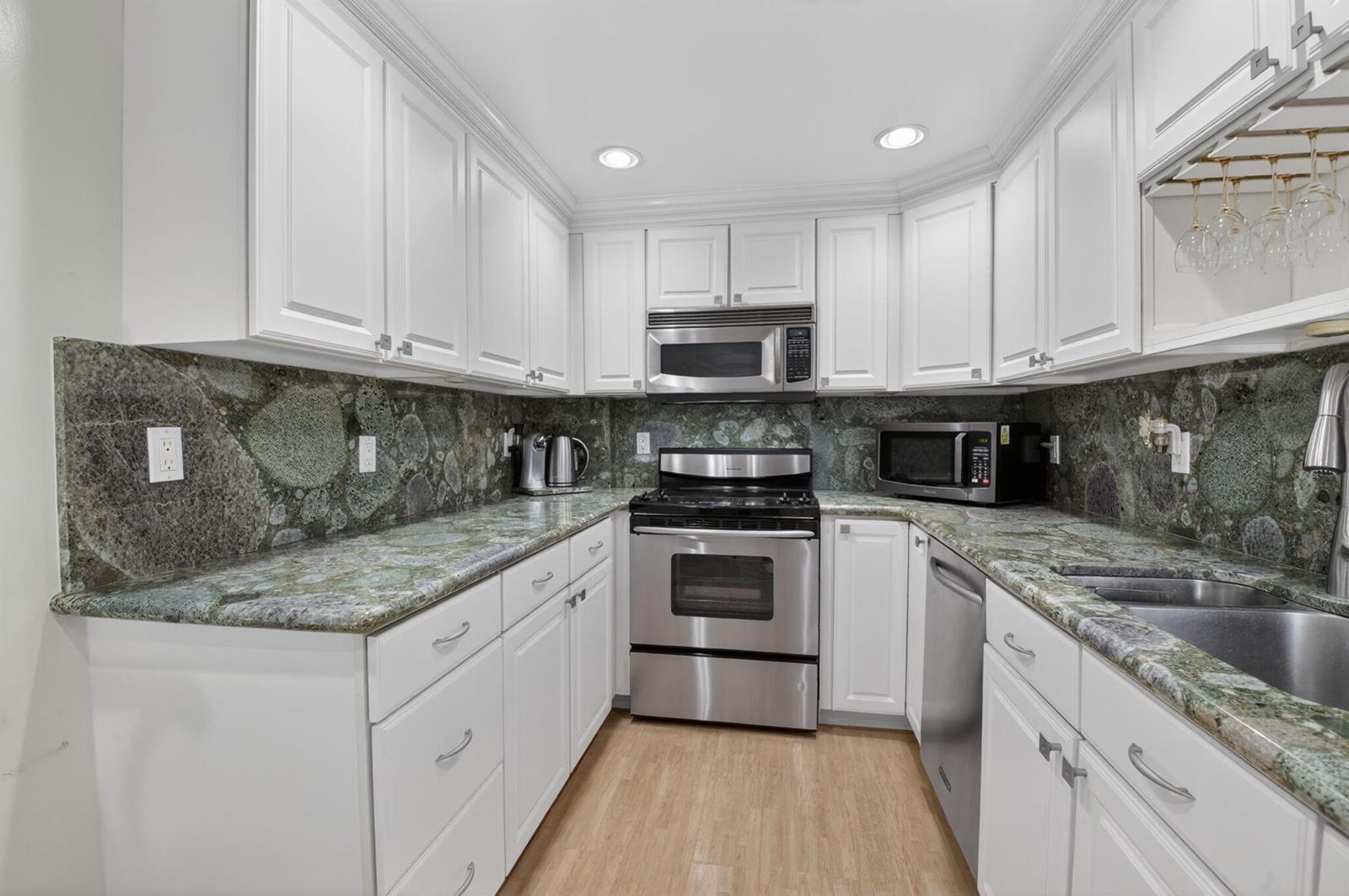 A kitchen features white cabinetry, stainless steel appliances, and green patterned stone countertops and backsplash — 2851 S Ocean Boulevard # 5m, Boca Raton FL 33432, BOCA RATON, FL