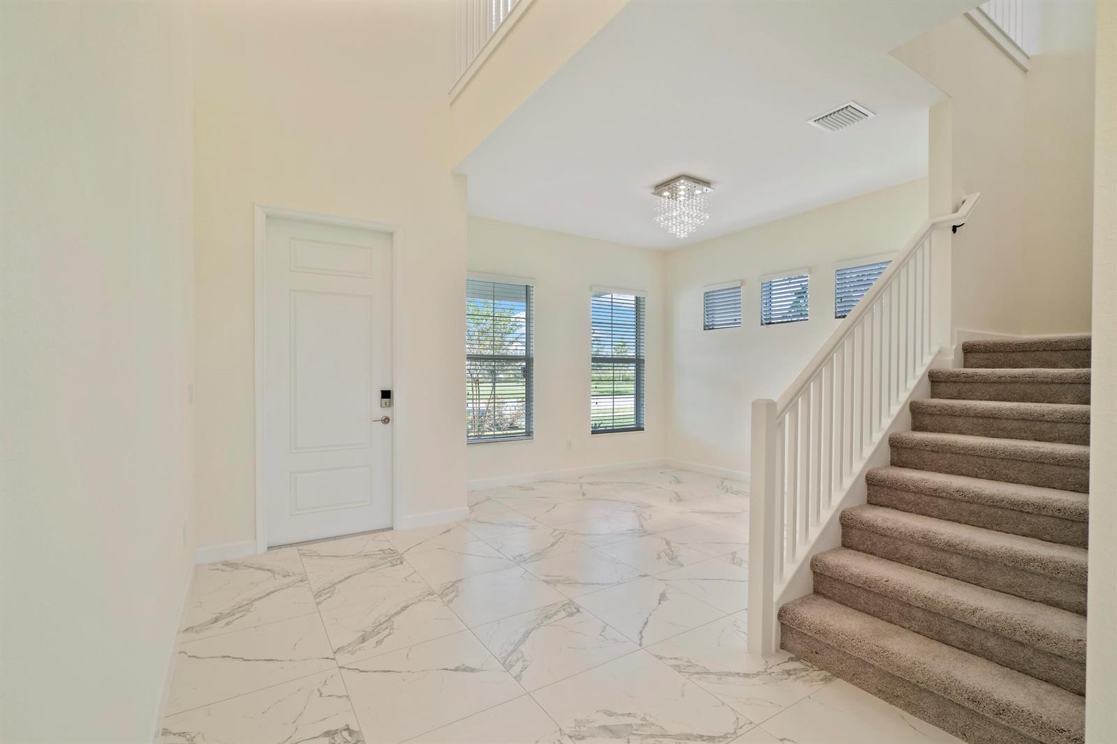A bright entryway features white marble-look tile flooring, a staircase with carpet, and a chandelier — 19551 Split Rail Run, Loxahatchee FL 33470, LOXAHATCHEE, FL