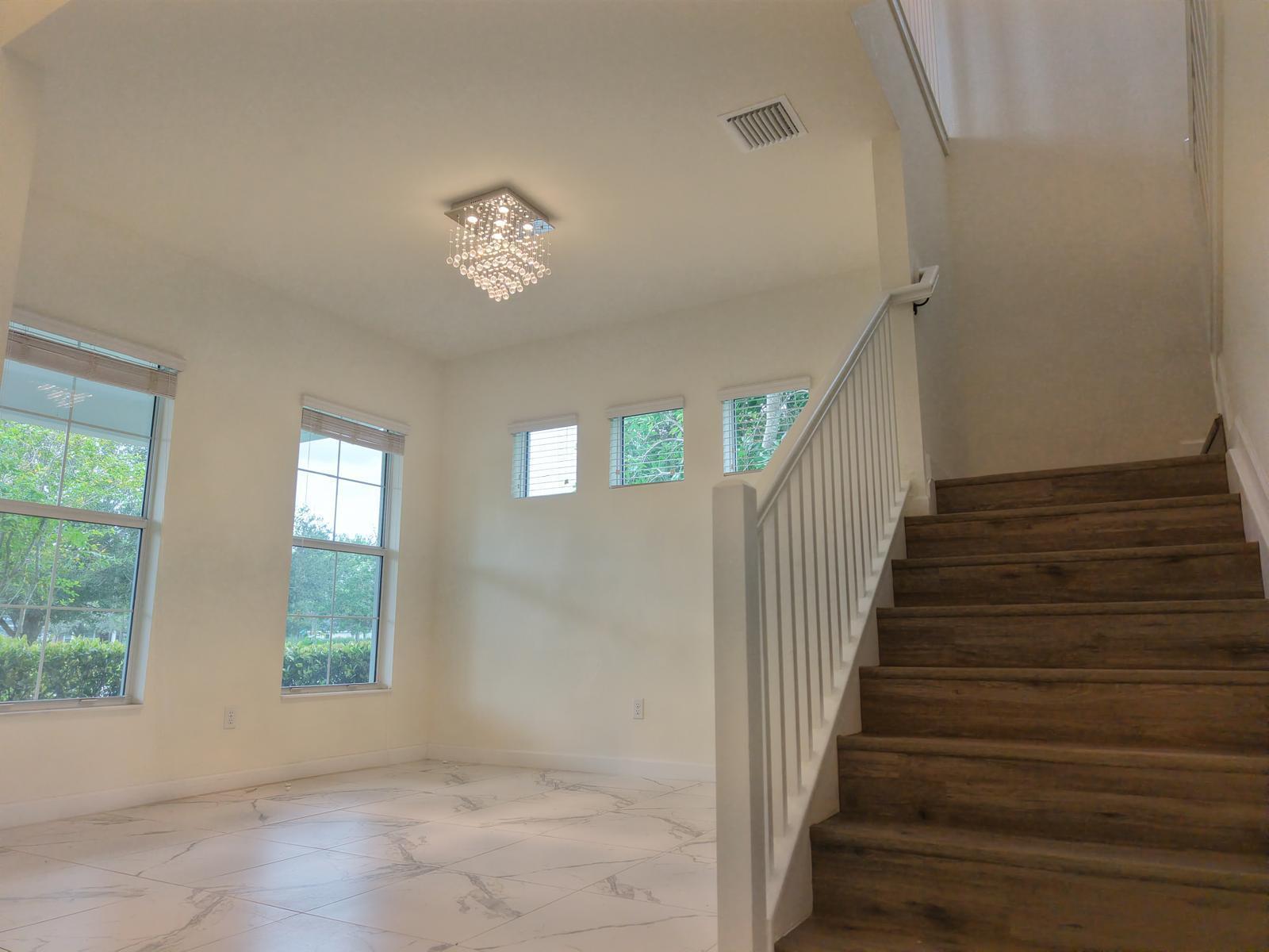 A bright foyer features white marble-look tile flooring, a crystal chandelier, and a wooden staircase — 19551 Split Rail Run, Loxahatchee FL 33470, LOXAHATCHEE, FL