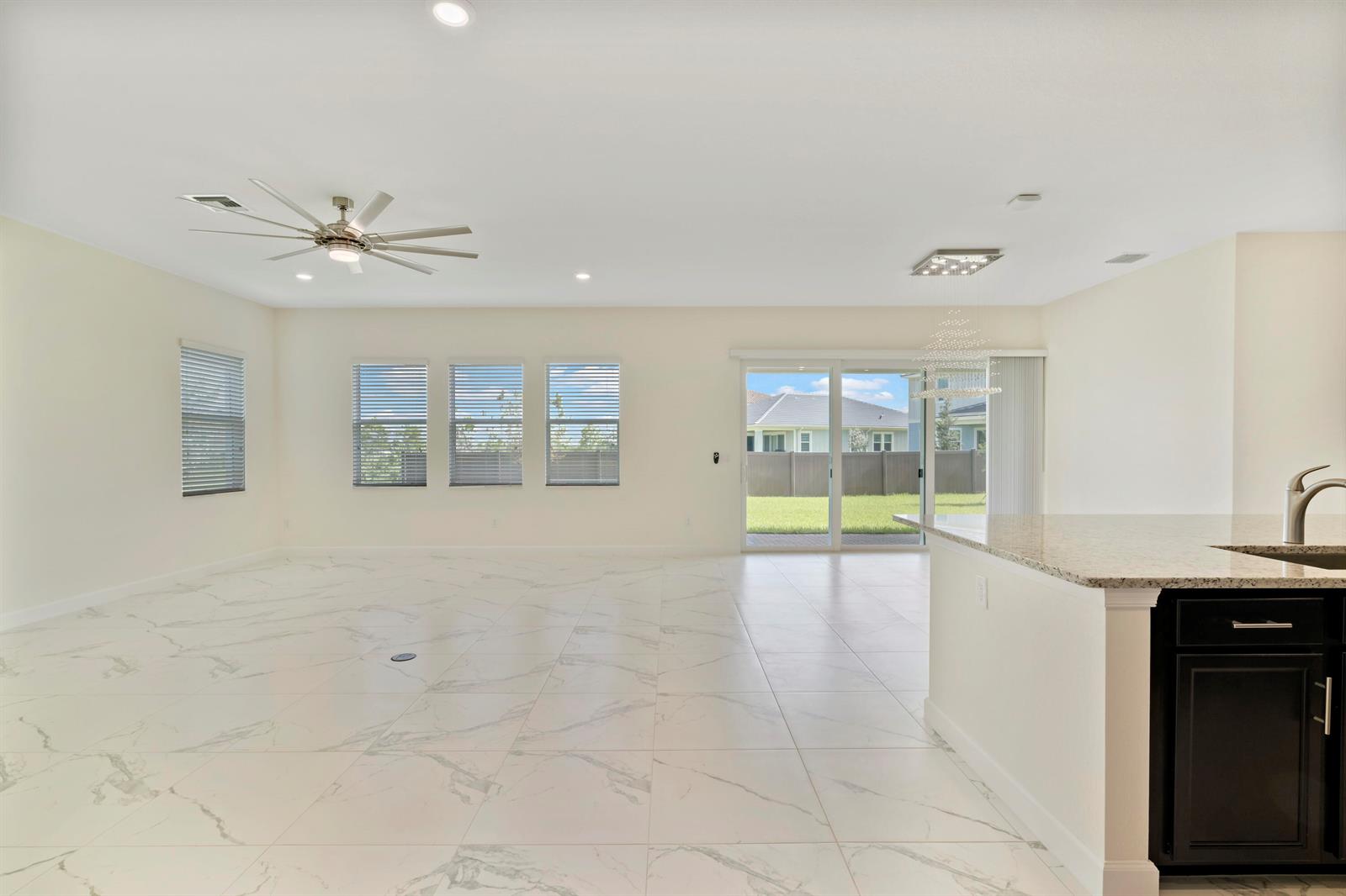 An open-concept living area features white marble-look tile flooring, a ceiling fan, and sliding doors — 19551 Split Rail Run, Loxahatchee FL 33470, LOXAHATCHEE, FL
