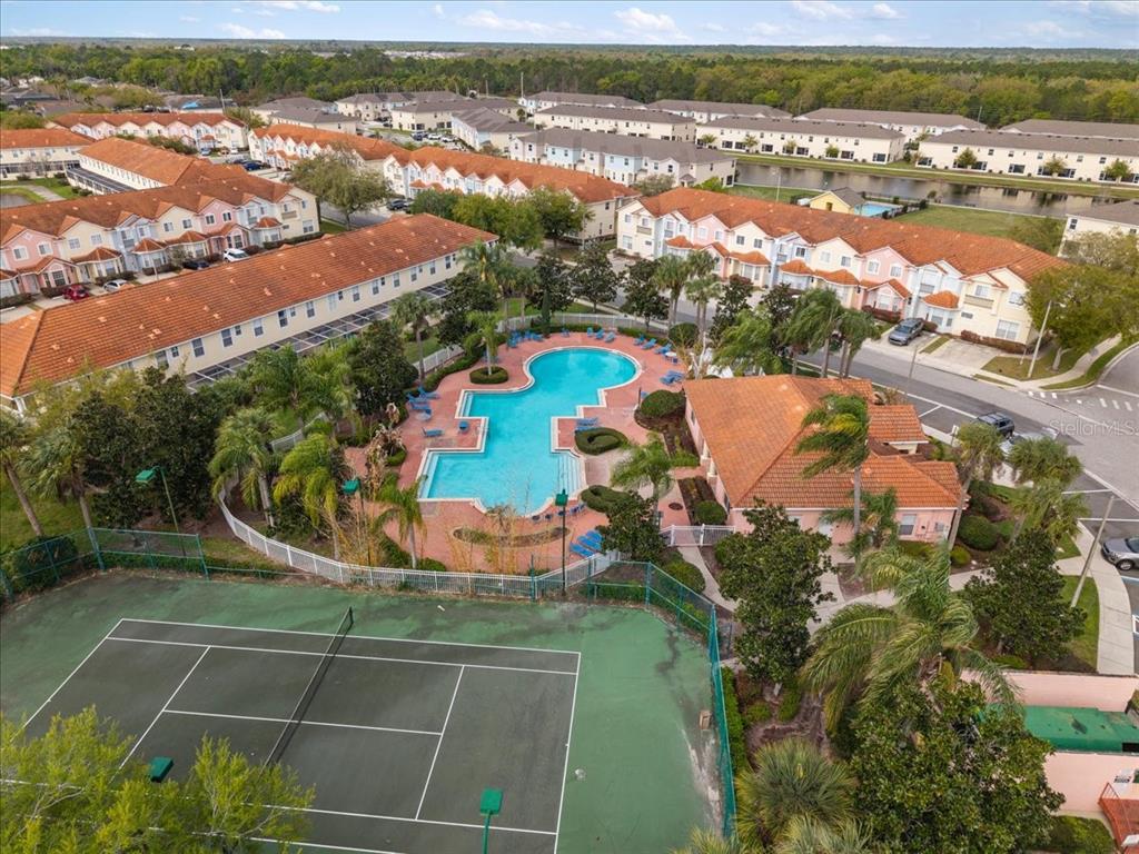 An aerial view shows a community swimming pool, a tennis court, and surrounding residential townhomes — 4855 CORAL CASTLE DRIVE, KISSIMMEE, FL