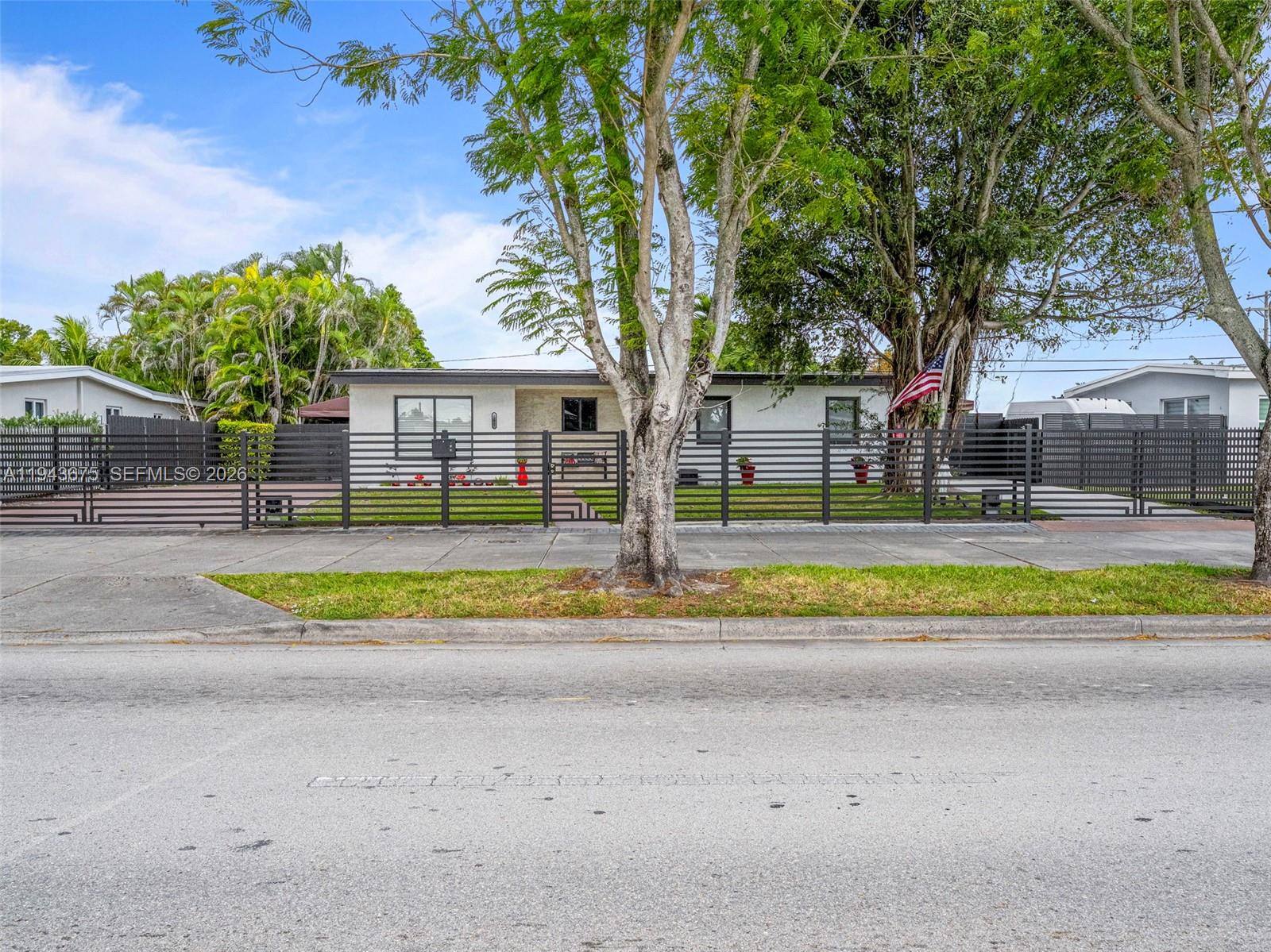 A single-story house with a horizontal slat fence and large trees in the front yard — 11415 SW 56th St, Miami FL 33165, MIAMI, FL