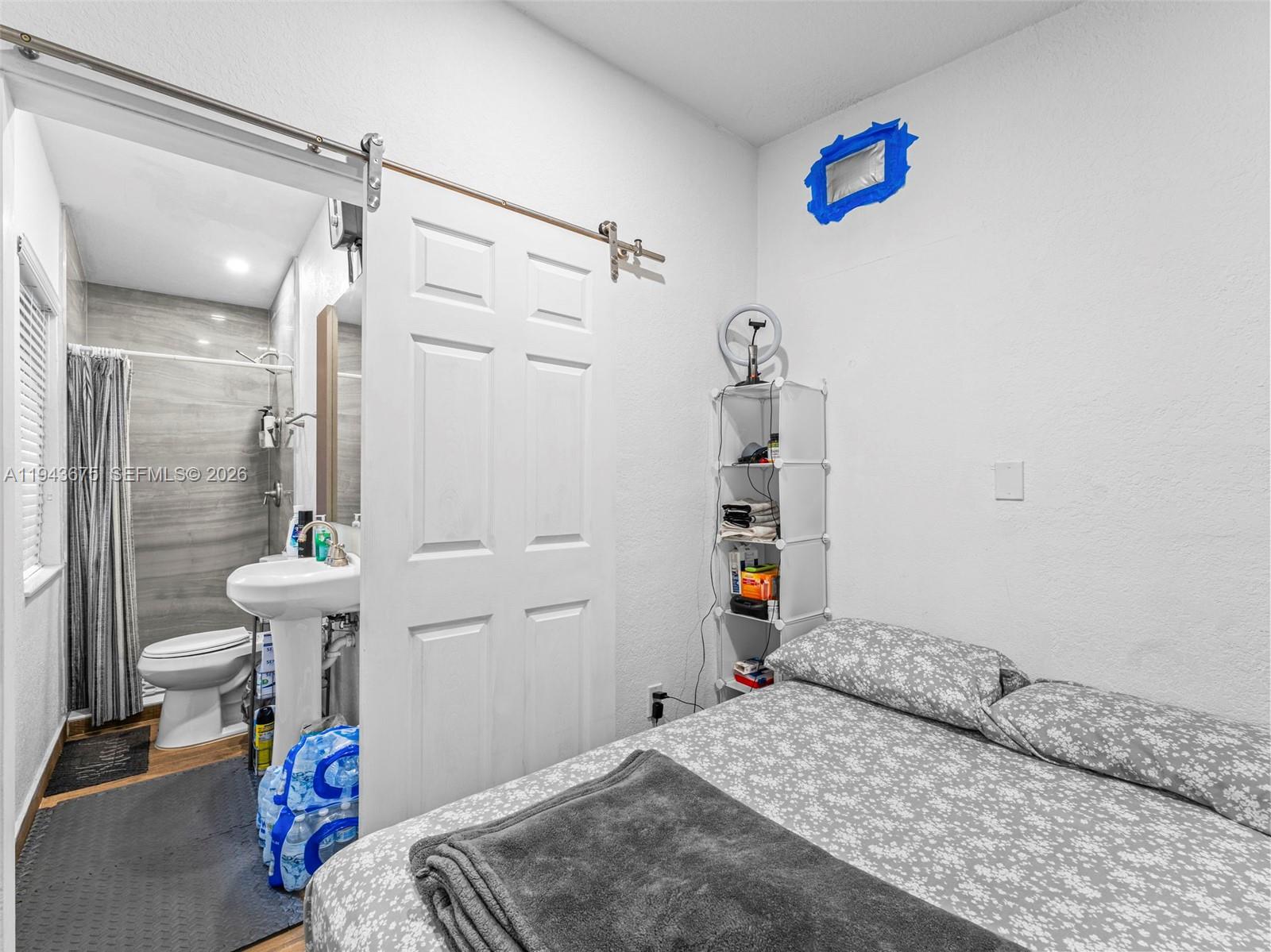 A bedroom with a bed and shelving unit features an attached bathroom behind a sliding door — 11415 SW 56th St, Miami FL 33165, MIAMI, FL