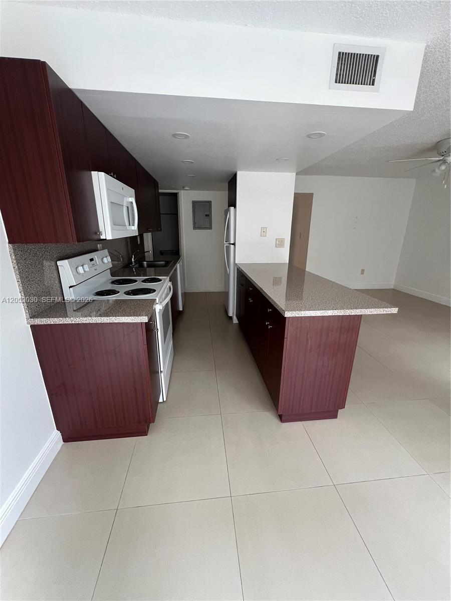 A kitchen features dark wood cabinets, granite countertops, white appliances, and light-colored tile flooring — 9310 W Flagler St # 115A, Miami FL 33174, MIAMI, FL