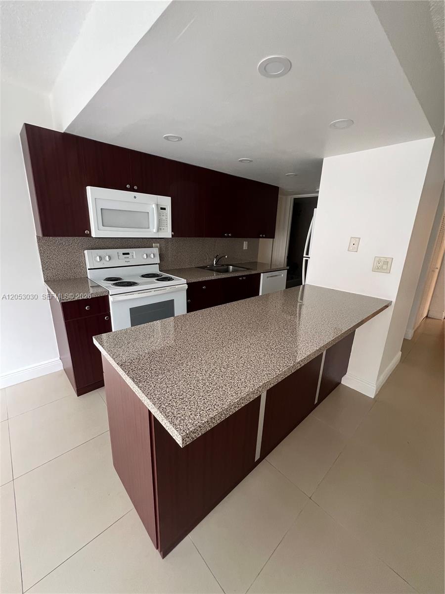 A kitchen features dark wood cabinets, granite countertops, and white appliances — 9310 W Flagler St # 115A, Miami FL 33174, MIAMI, FL