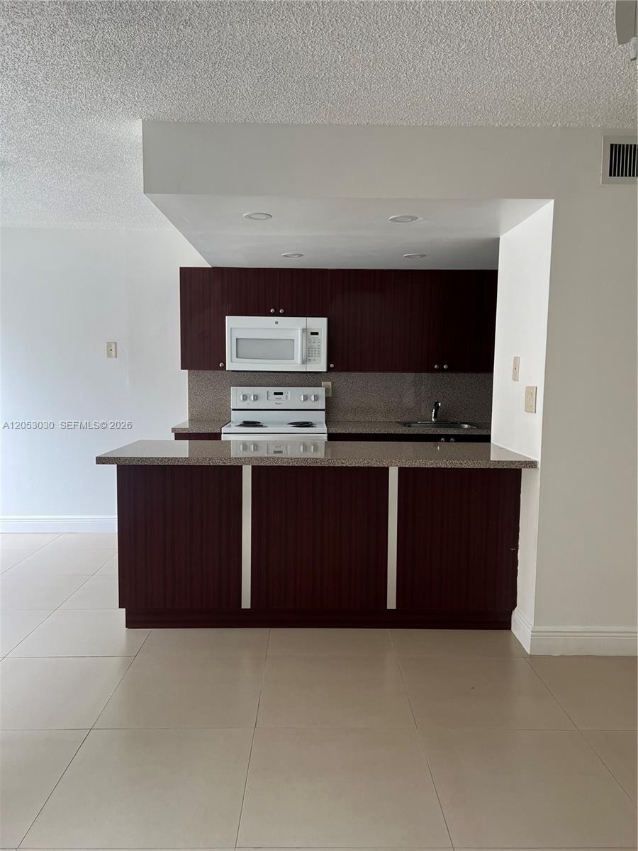 A kitchen features dark wood cabinets, a speckled countertop, and white appliances — 9310 W Flagler St # 115A, Miami FL 33174, MIAMI, FL