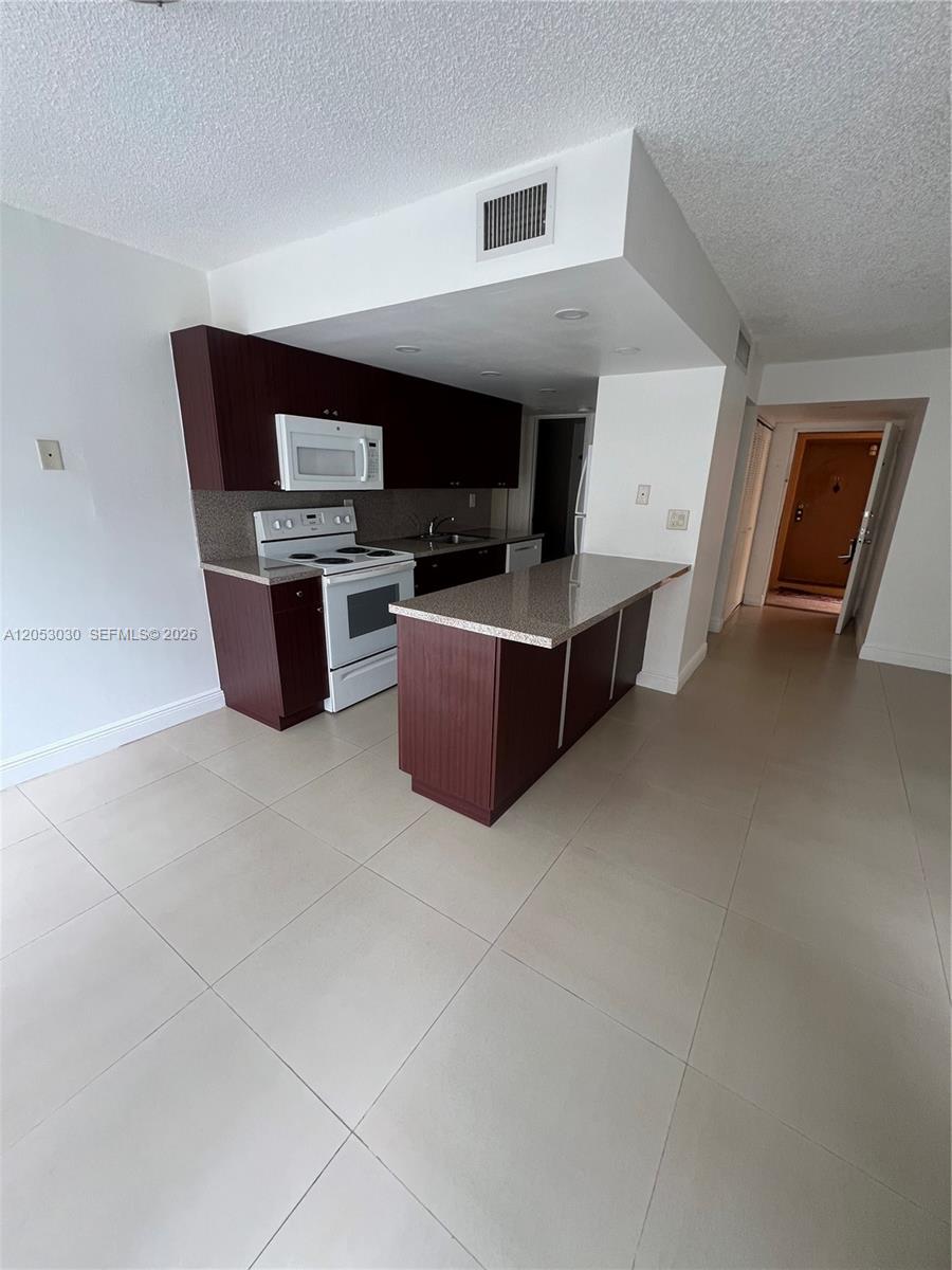 A kitchen features dark wood cabinets, a white stove, and a granite-topped island — 9310 W Flagler St # 115A, Miami FL 33174, MIAMI, FL