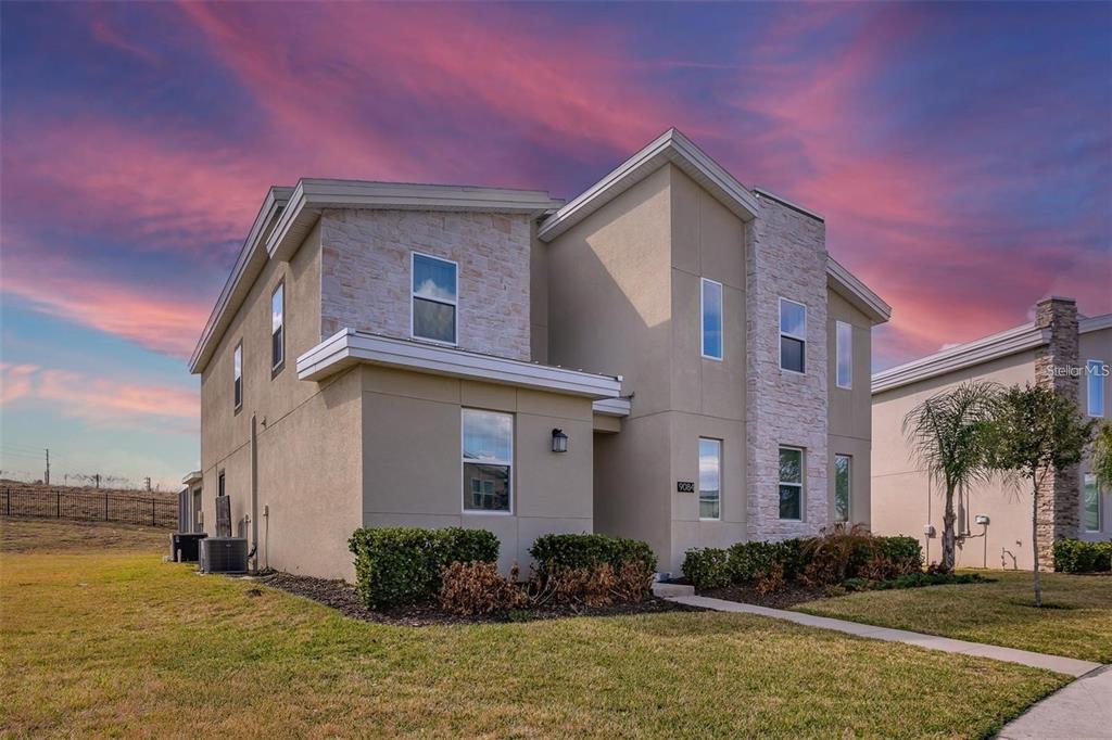 A two-story house with tan stucco and stone veneer siding under a sunset sky — 9084 SOMMERSET HILLS DRIVE, DAVENPORT, FL