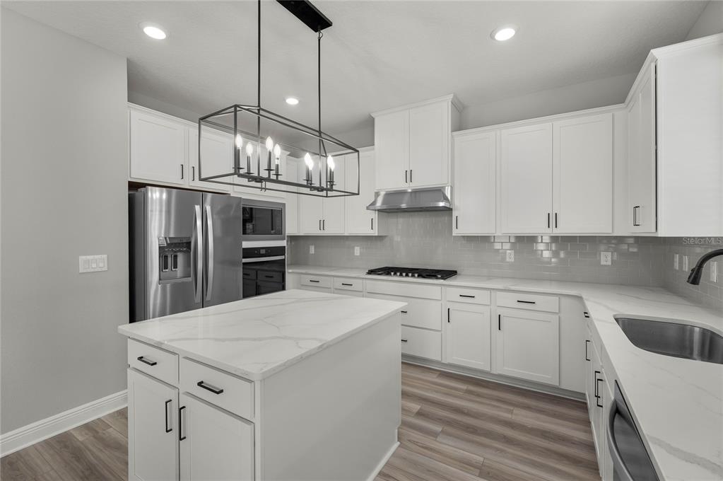 A modern kitchen features white cabinets, a marble-topped island, stainless steel appliances, and gray flooring — 7829 MARLOW PLACE, KISSIMMEE, FL