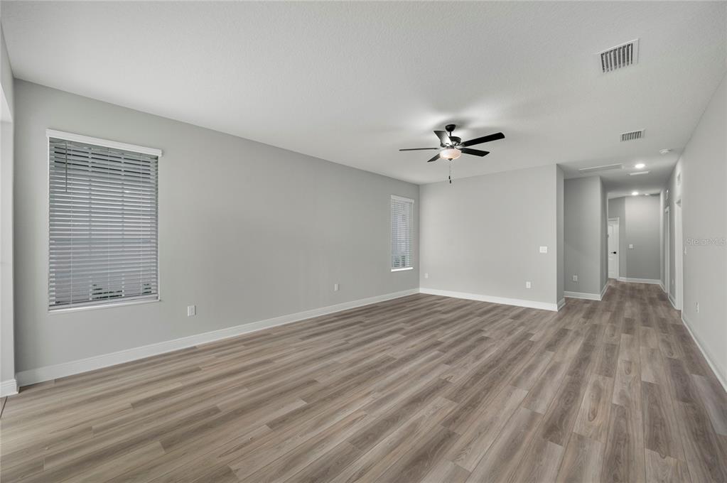 An empty living room with light gray walls, wood-look flooring, and a ceiling fan — 7829 MARLOW PLACE, KISSIMMEE, FL