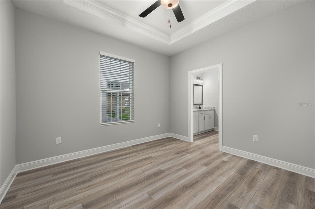 A bedroom with gray walls, wood-look flooring, a tray ceiling, and an attached bathroom — 7829 MARLOW PLACE, KISSIMMEE, FL