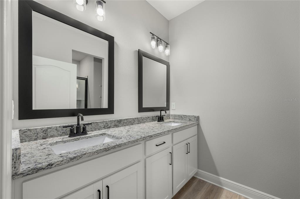 A bathroom features a double vanity with white cabinets, granite countertops, and black framed mirrors — 7829 MARLOW PLACE, KISSIMMEE, FL