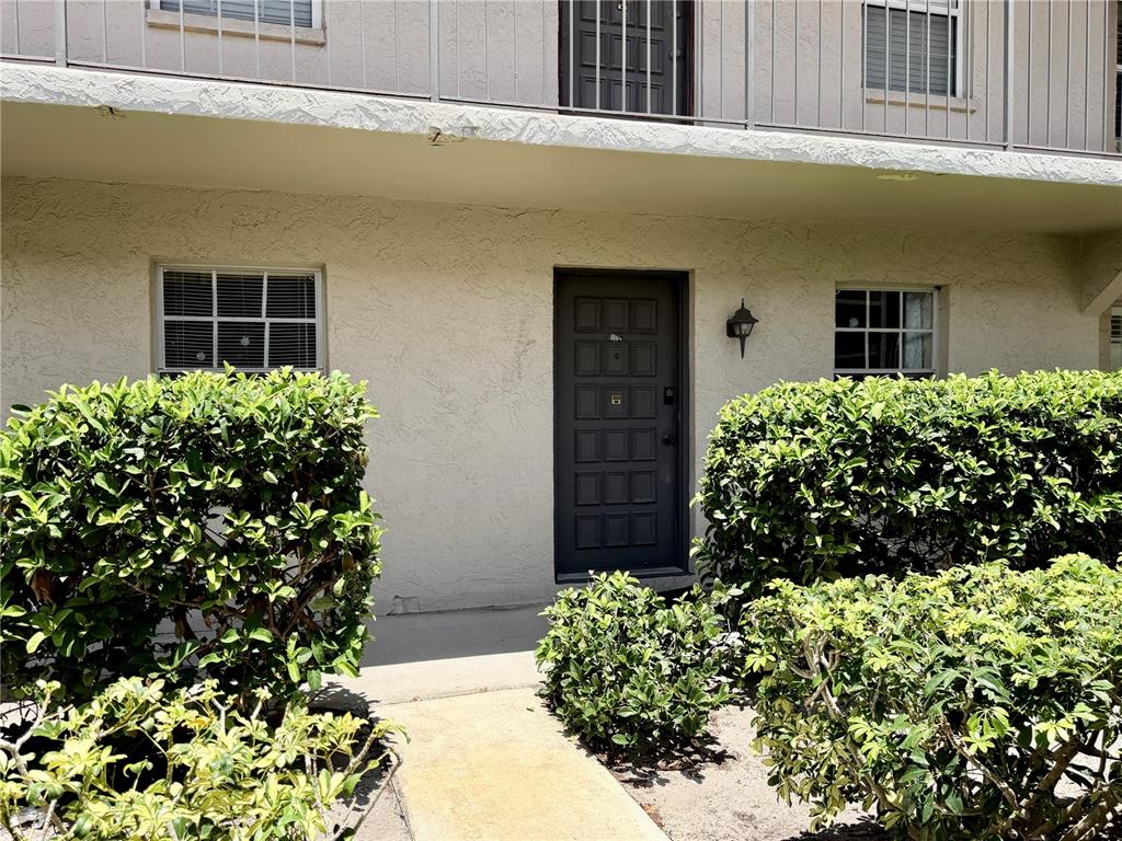 A ground-level apartment entrance features a dark door flanked by windows and green bushes — 8703 BARDMOOR BOULEVARD UNIT 102, SEMINOLE, FL
