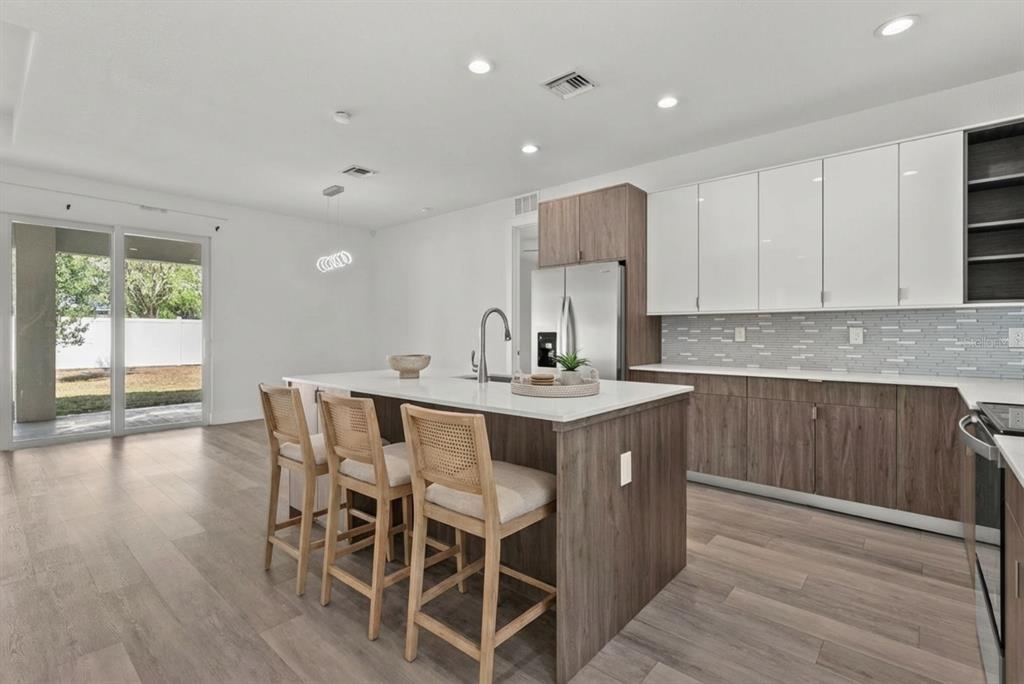 A modern kitchen features a wood-toned island with bar stools, white upper cabinets, and tile backsplash — 2711 ATWATER DRIVE, NORTH PORT, FL