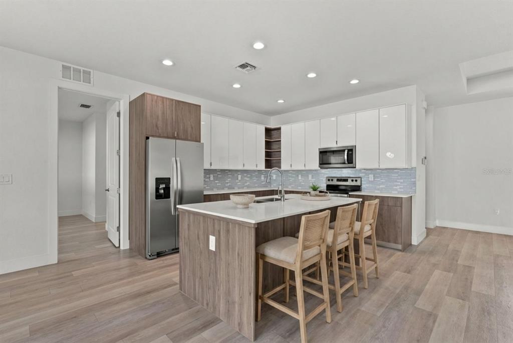 A modern kitchen features a central island, white upper cabinets, wood-tone lower cabinets, and stainless appliances — 2711 ATWATER DRIVE, NORTH PORT, FL