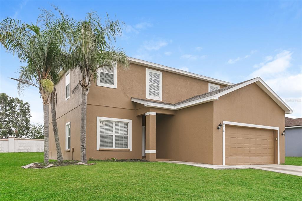 A two-story tan house with a two-car garage and a palm tree in the yard — 8870 PEBBLEBROOKE DRIVE, LAKELAND, FL