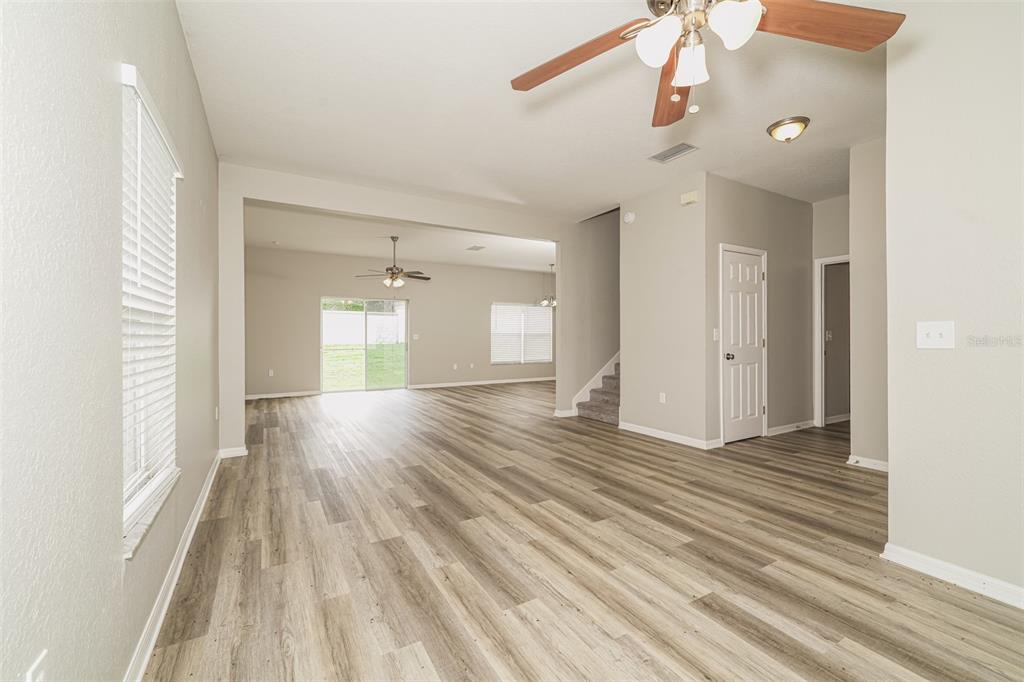 An open-concept living area features light wood-look flooring, neutral walls, and a ceiling fan — 8870 PEBBLEBROOKE DRIVE, LAKELAND, FL