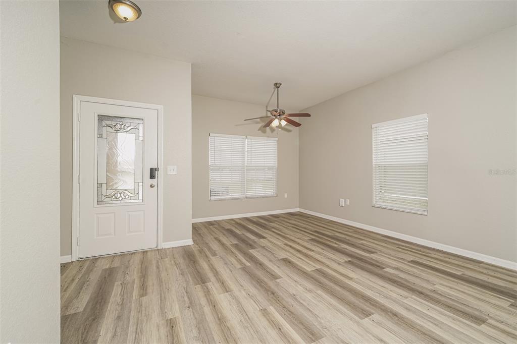 An empty room features light gray walls, wood-look flooring, a ceiling fan, and a front door — 8870 PEBBLEBROOKE DRIVE, LAKELAND, FL