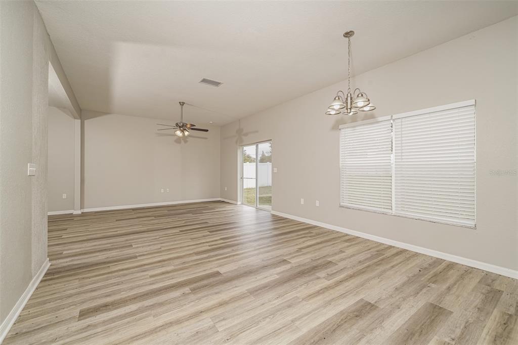 An open-concept living and dining area features light wood-look flooring, a ceiling fan, and chandelier — 8870 PEBBLEBROOKE DRIVE, LAKELAND, FL
