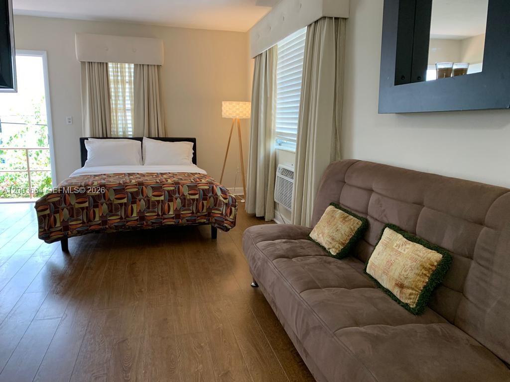 A bedroom features a bed with a patterned comforter, a brown sofa, and wood flooring — 740 Michigan Ave # 10, Miami Beach FL 33139, MIAMI BEACH, FL