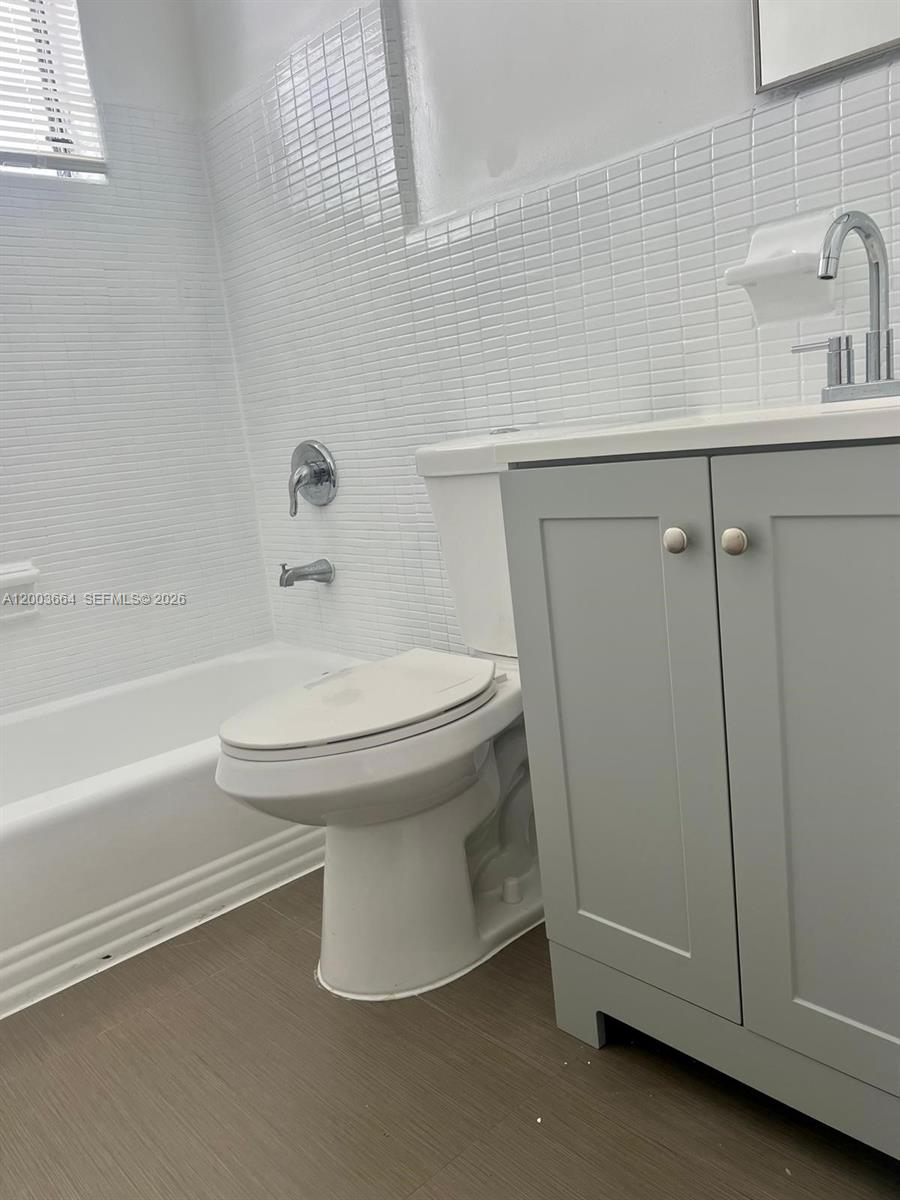 A bathroom features a white bathtub, a toilet, and a grey vanity with a sink — 740 Michigan Ave # 10, Miami Beach FL 33139, MIAMI BEACH, FL