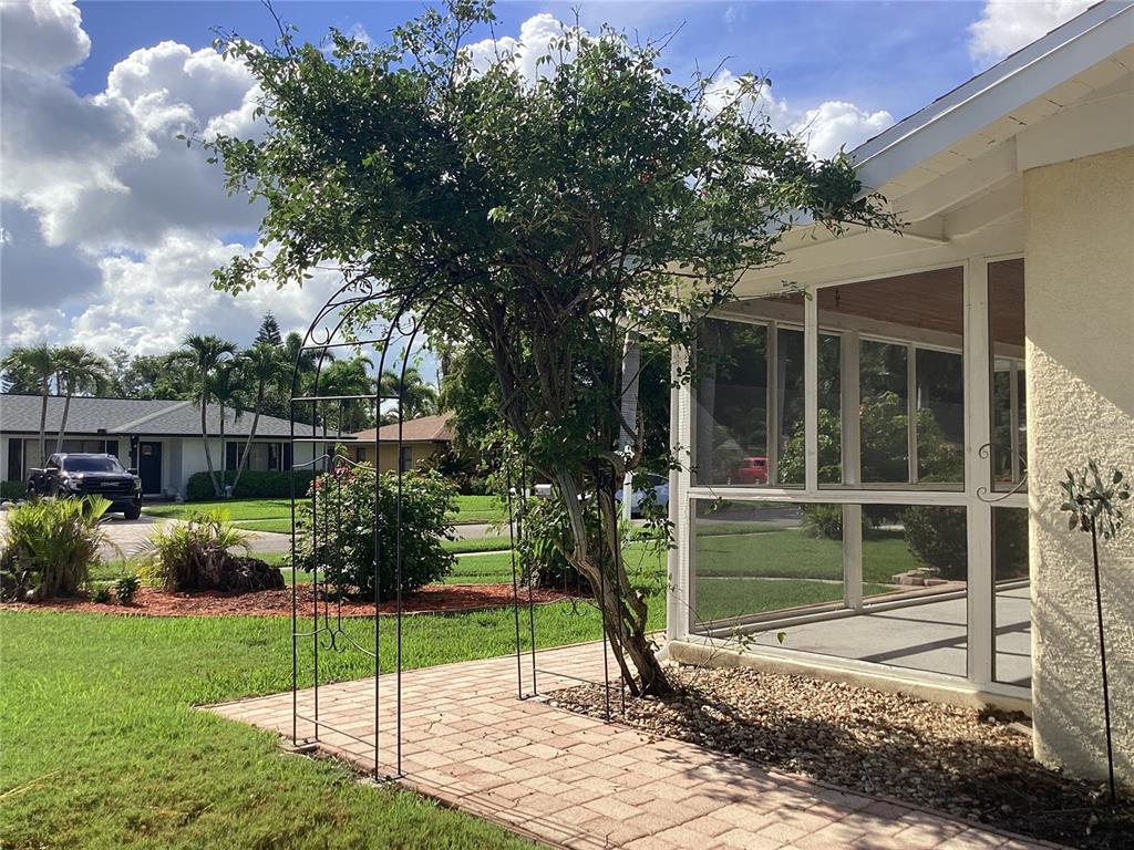 A metal garden arch stands over a paver walkway beside a screened-in porch — 710 50TH STREET COURT W, BRADENTON, FL