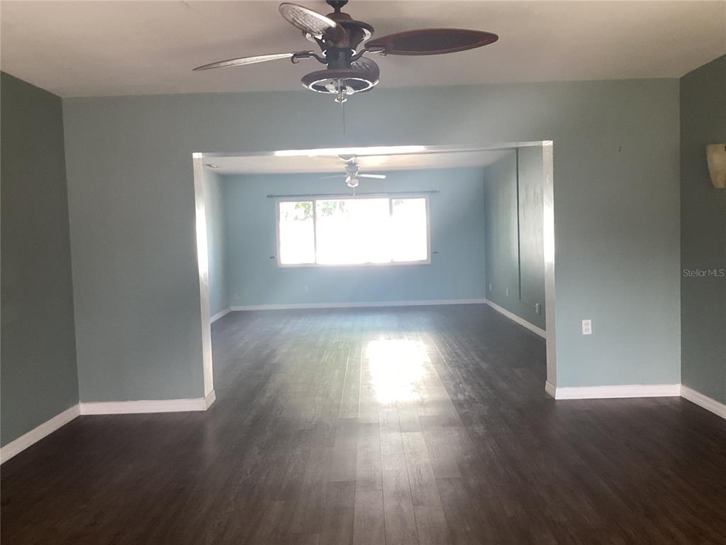 A living area with dark wood-look flooring and a ceiling fan leads to another room — 710 50TH STREET COURT W, BRADENTON, FL