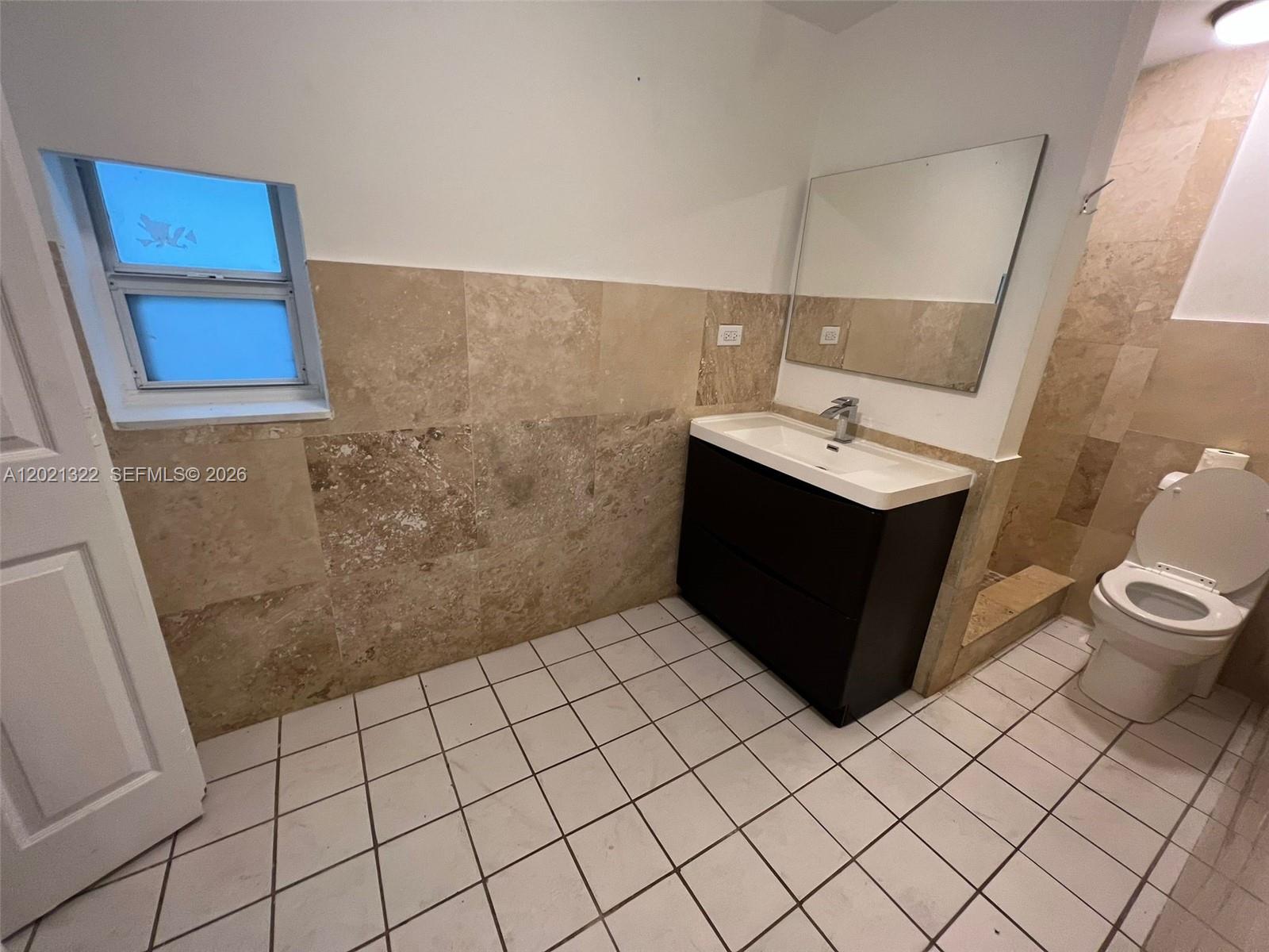 A bathroom features a dark vanity, a wall-mounted mirror, a toilet, and tiled walls — 644 NE 82nd Ter # 1, Miami FL 33138, MIAMI, FL