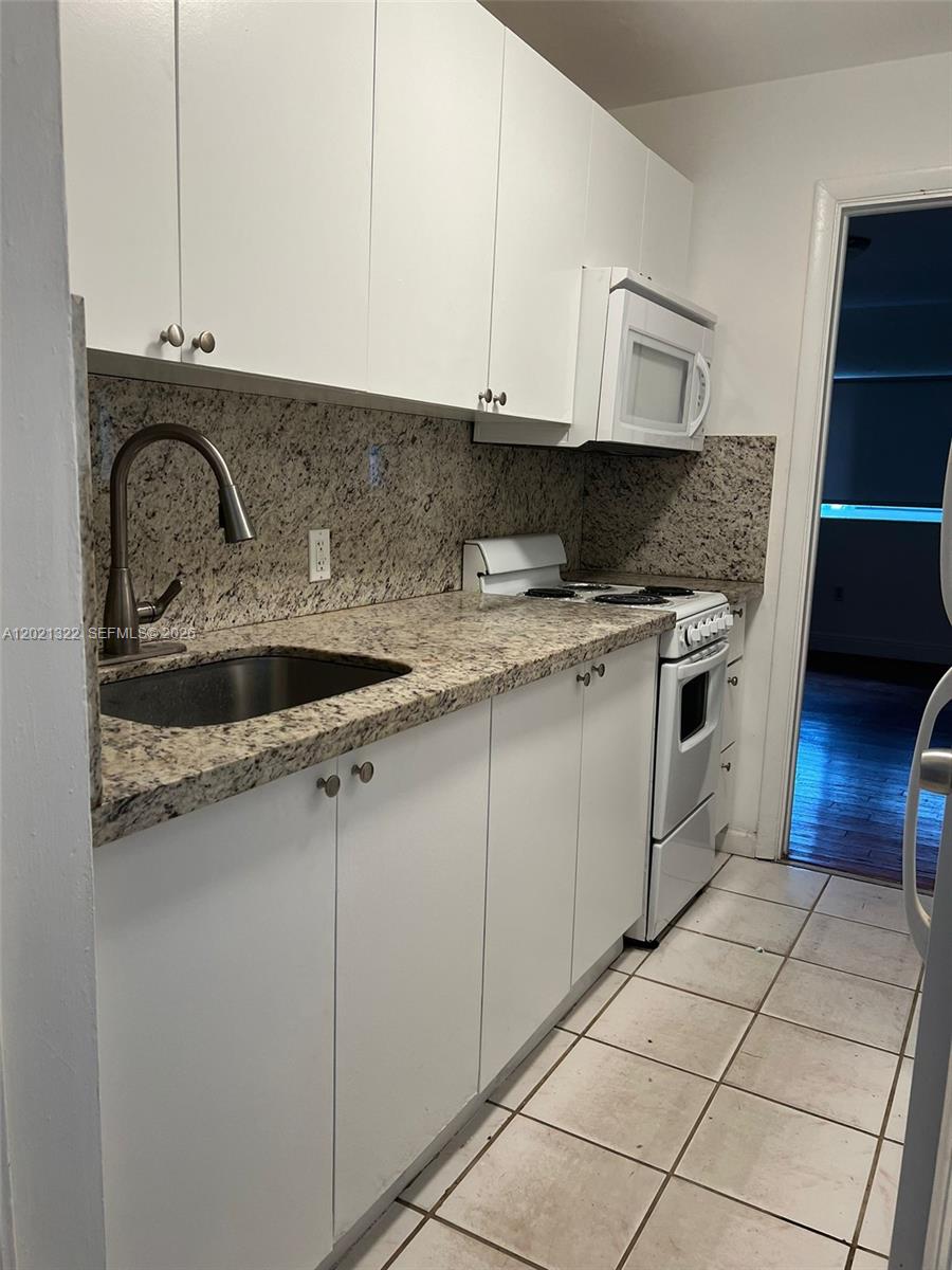 A small kitchen features white cabinets, granite countertops, a stainless steel sink, and white appliances — 644 NE 82nd Ter # 1, Miami FL 33138, MIAMI, FL