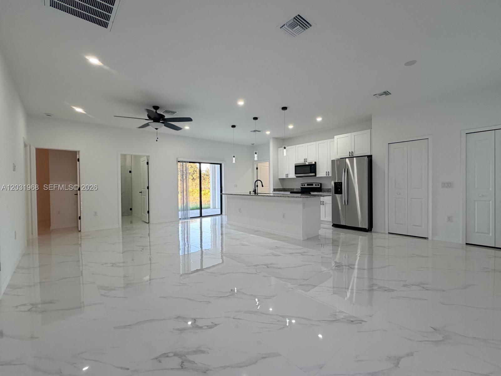 An open-concept kitchen and living area features white cabinetry, stainless steel appliances, and marble-look flooring — 2706 72nd St W, Lehigh Acres FL 33971, LEHIGH ACRES, FL