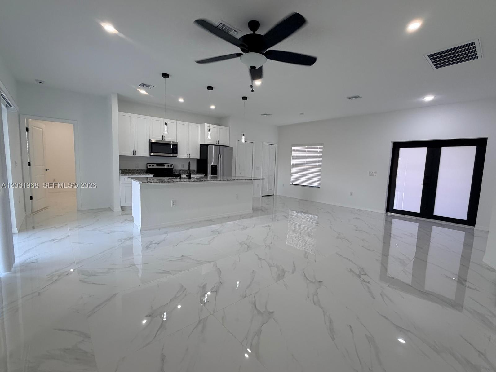 A modern kitchen with white cabinets and a marble-patterned floor opens to a living area — 2706 72nd St W, Lehigh Acres FL 33971, LEHIGH ACRES, FL