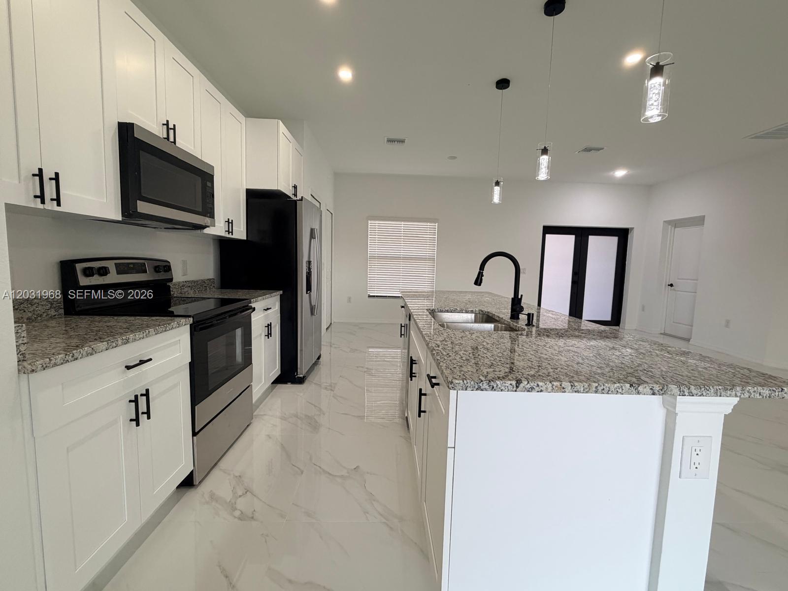 A modern kitchen features white cabinets, granite countertops, stainless steel appliances, and a large island — 2706 72nd St W, Lehigh Acres FL 33971, LEHIGH ACRES, FL