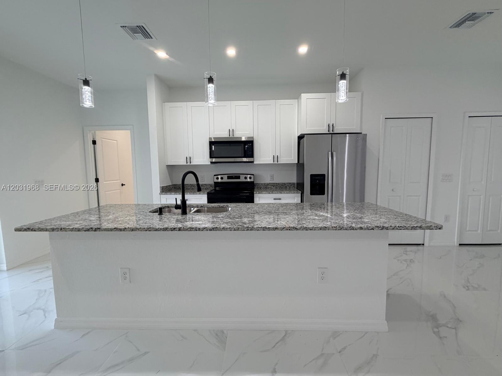 A kitchen features white cabinets, granite countertops, a large island, and stainless steel appliances — 2706 72nd St W, Lehigh Acres FL 33971, LEHIGH ACRES, FL