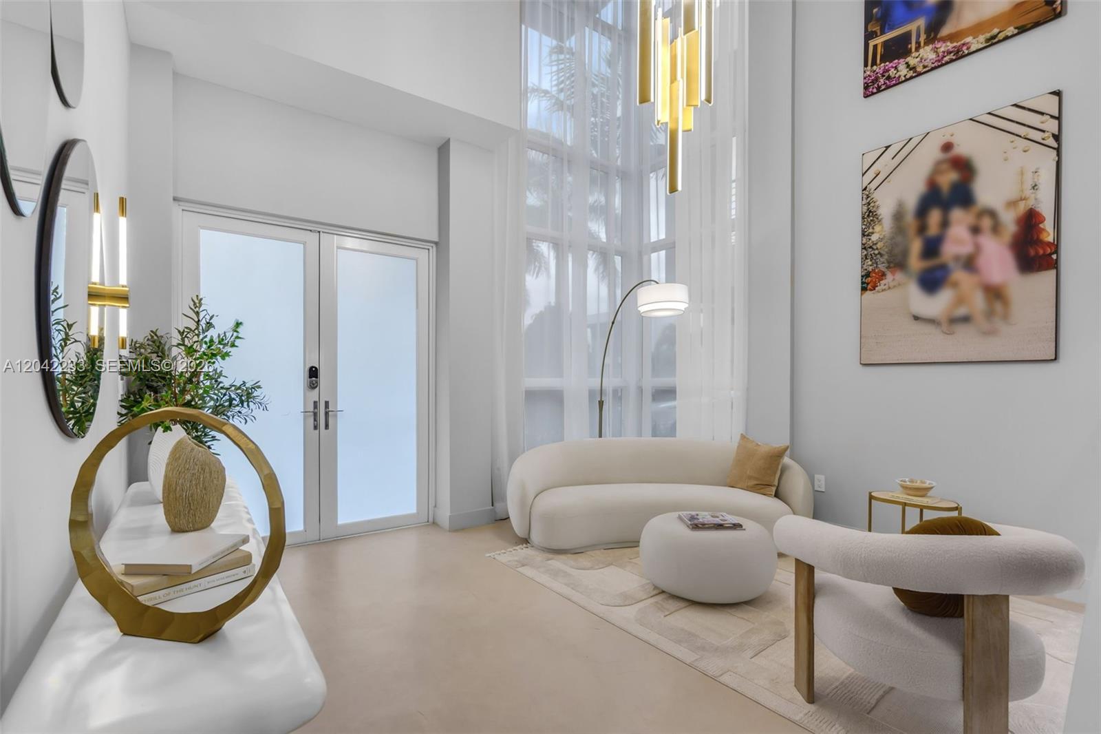 A bright living room features a curved sofa, tall windows, and a modern gold chandelier — 7533 NW 98th Ct, Doral FL 33178, DORAL, FL