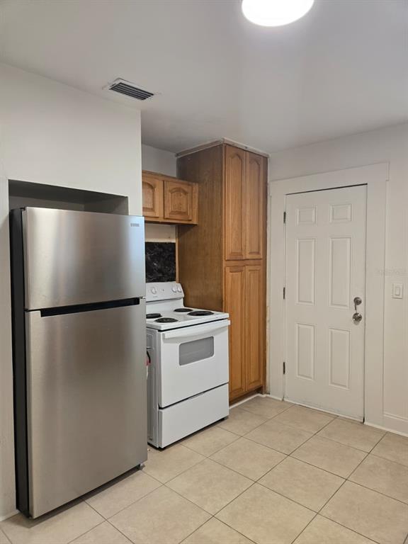 A kitchen features a stainless steel refrigerator, white stove, wooden cabinets, and tiled flooring — 709 E JAMES STREET, TAMPA, FL